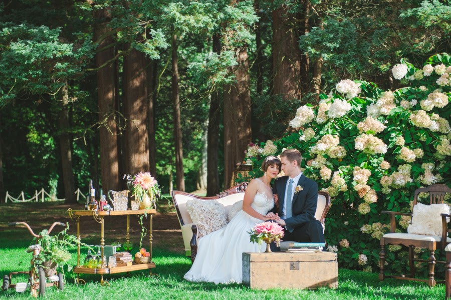 Bride and groom sit together on Victorian loveseat with other vintage style furniture outdoors